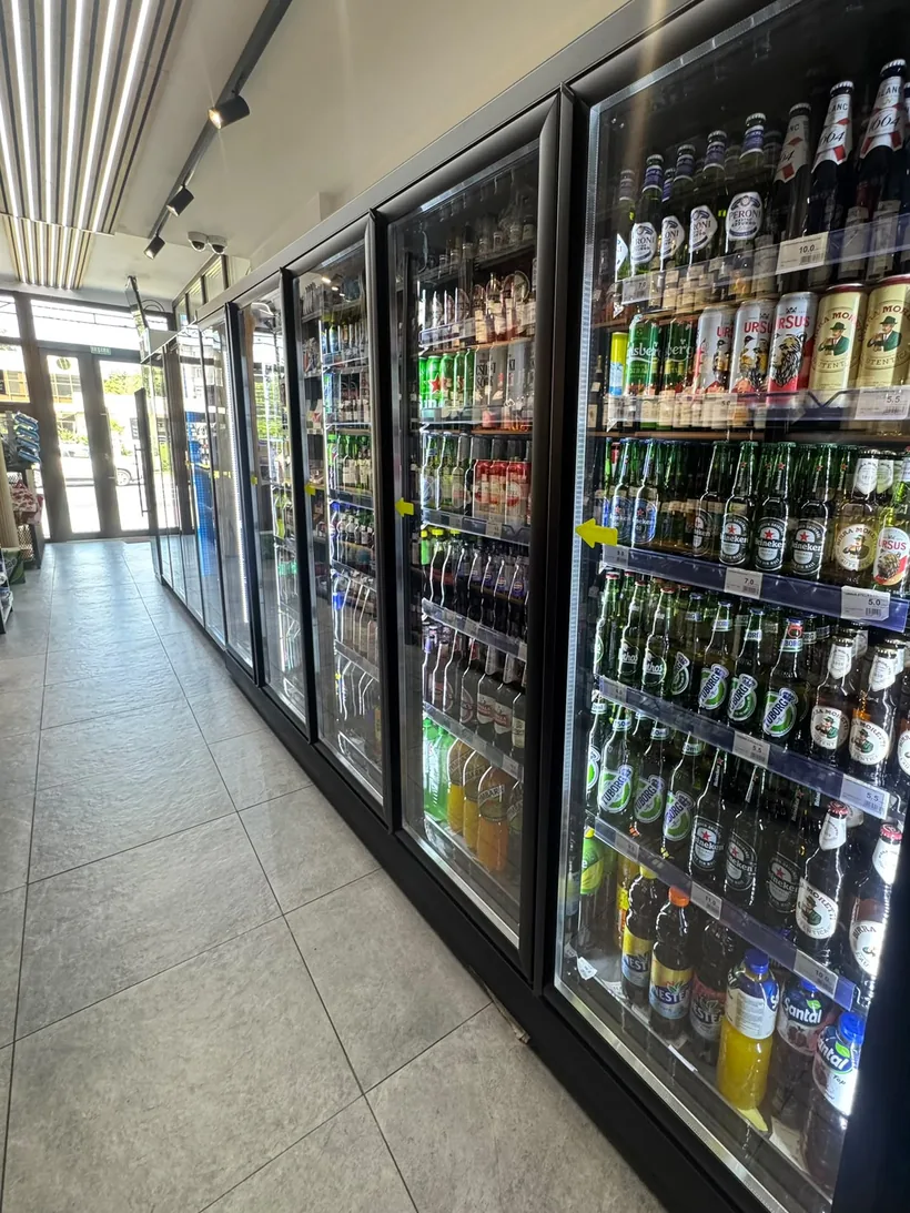 Culoarul magazinului 4Drinks, cu vitrine frigorifice și peretele de vinuri